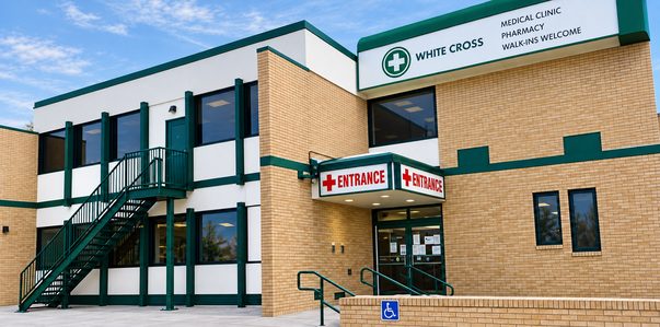 The White Cross Healthcare building at 647 Broadway in Winnipeg: a two-storey tan brick building with a green-trimmed White Cross sign and a covered entrance.